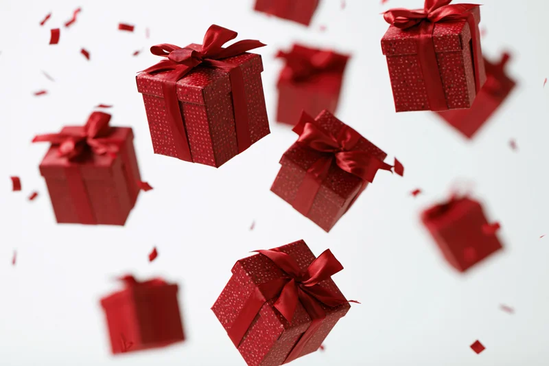 Red gift boxes with satin ribbon bows floating and tumbling in midair against white background with scattered confetti