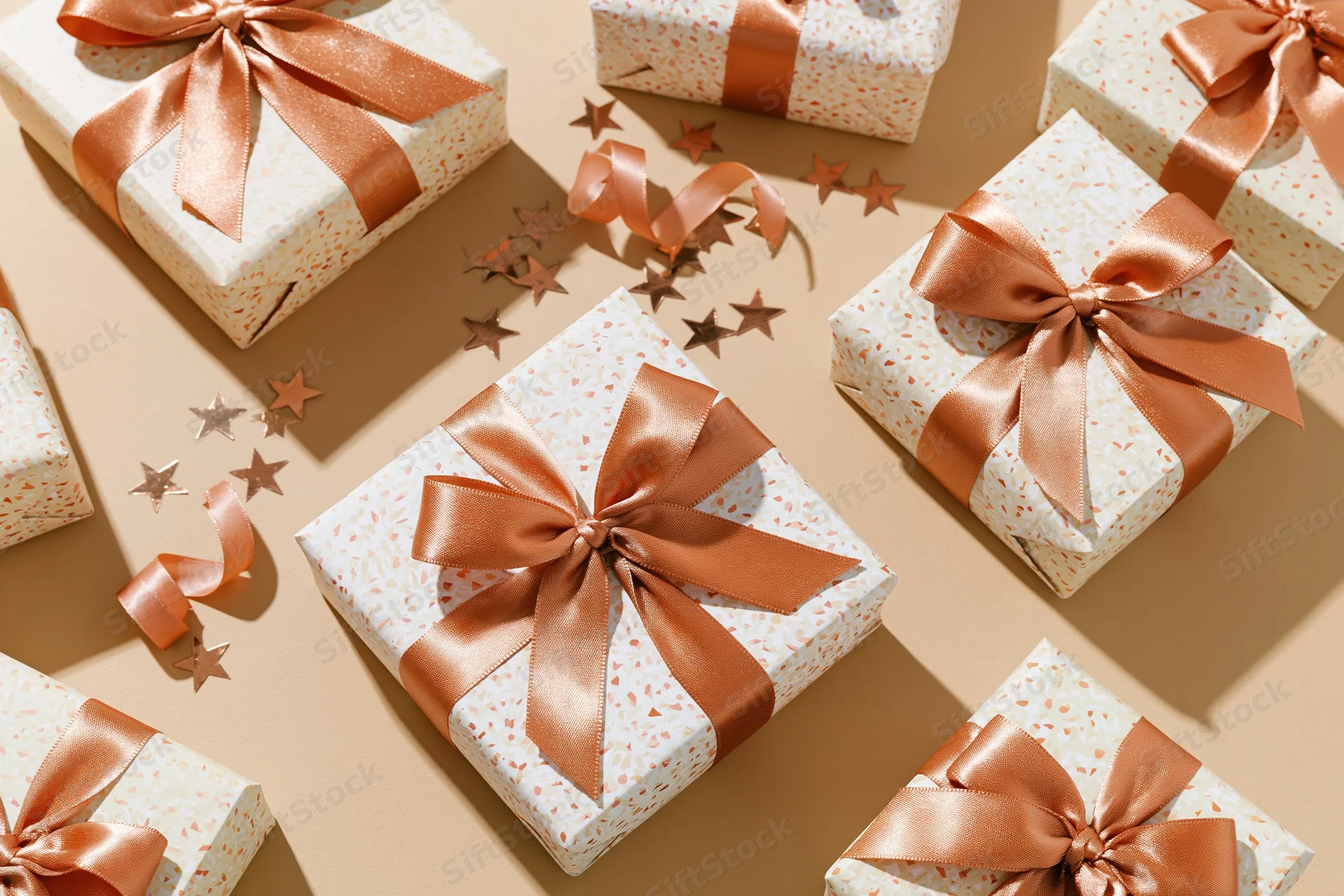 Wrapped gift boxes with copper ribbons and star confetti on beige surface