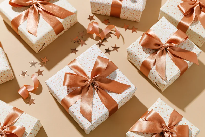 Wrapped gift boxes with copper ribbons and star confetti on beige surface