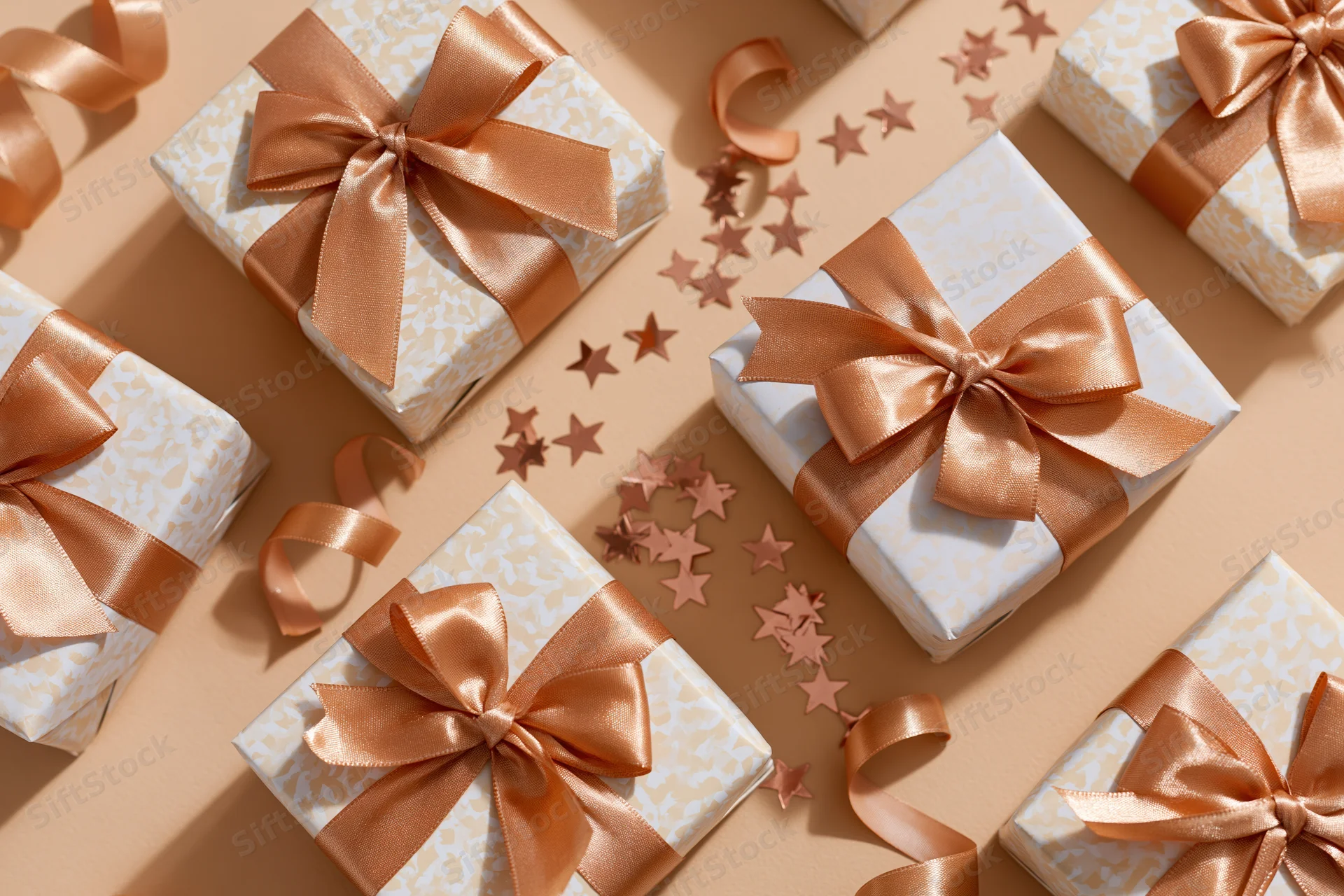 Gift boxes wrapped in patterned paper with satin ribbons arranged on beige surface with star confetti