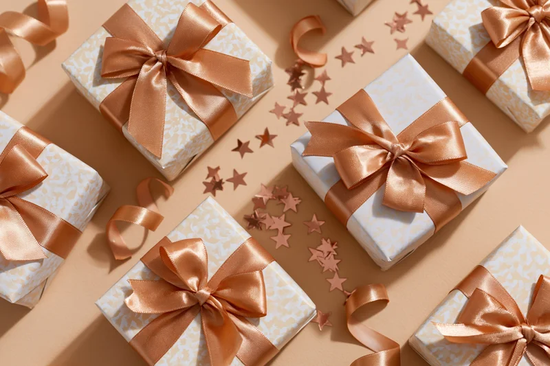 Gift boxes wrapped in patterned paper with satin ribbons arranged on beige surface with star confetti