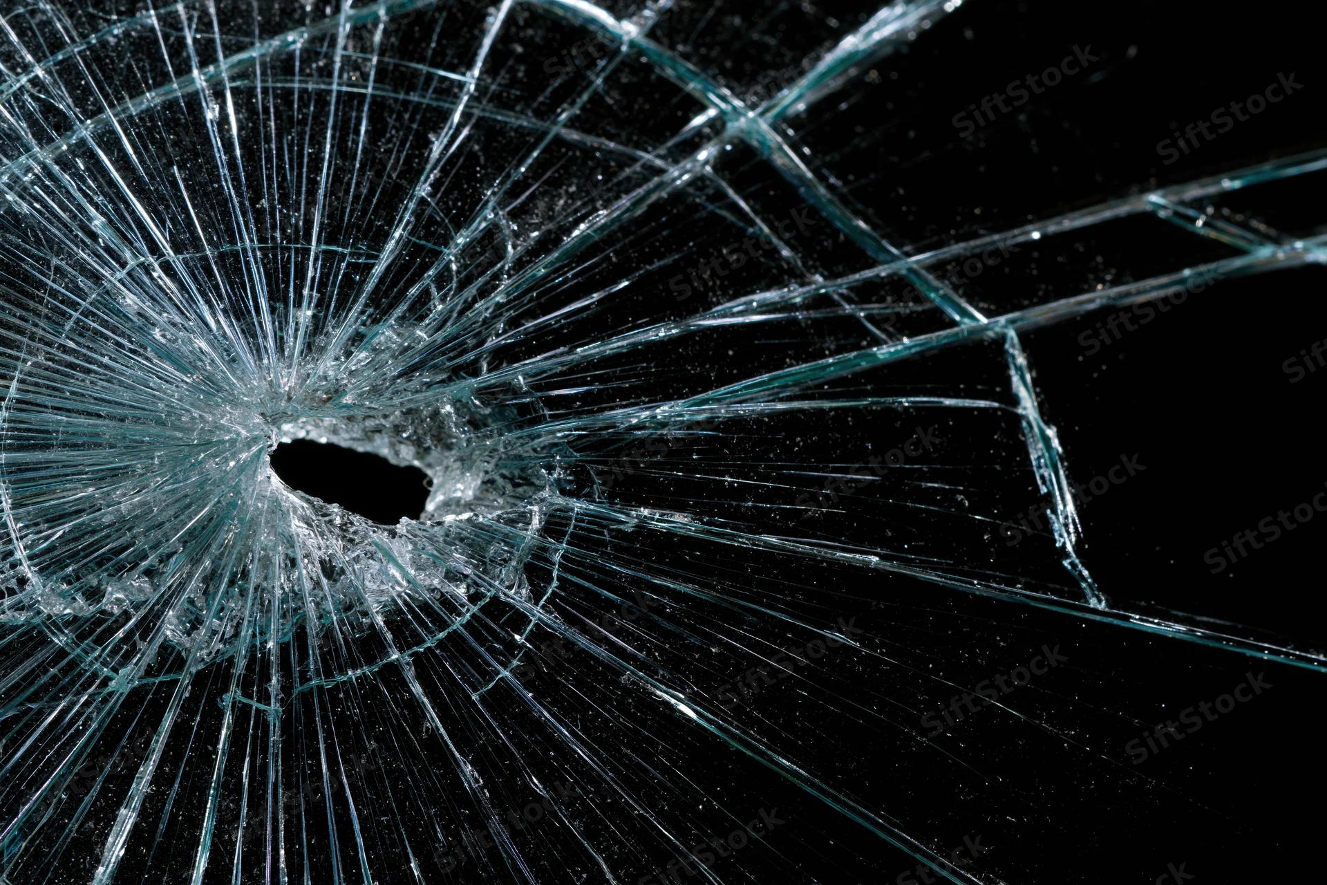 Shattered glass pane with central impact hole and radiating cracks against dark background