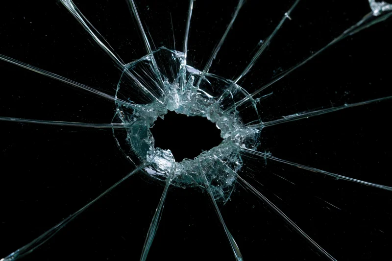 Shattered glass pane with central hole and radial cracks against black background