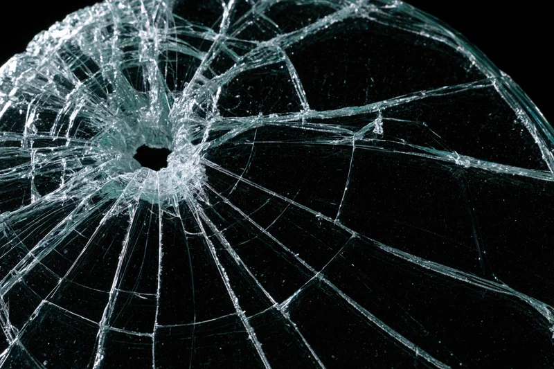 Shattered glass pane with central hole and radiating cracks against black background