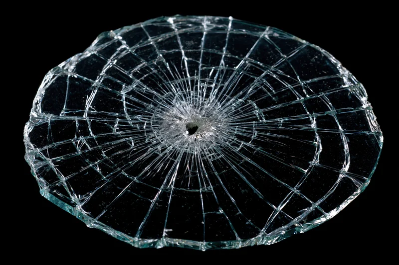 Shattered glass pane with radial cracks from central impact point on black background
