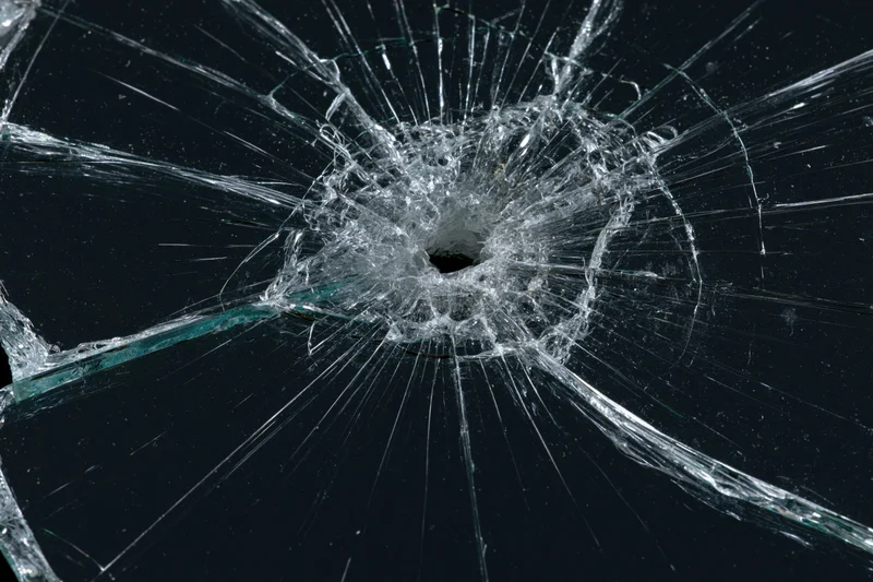 Shattered glass pane with central impact hole and radial cracks against dark background