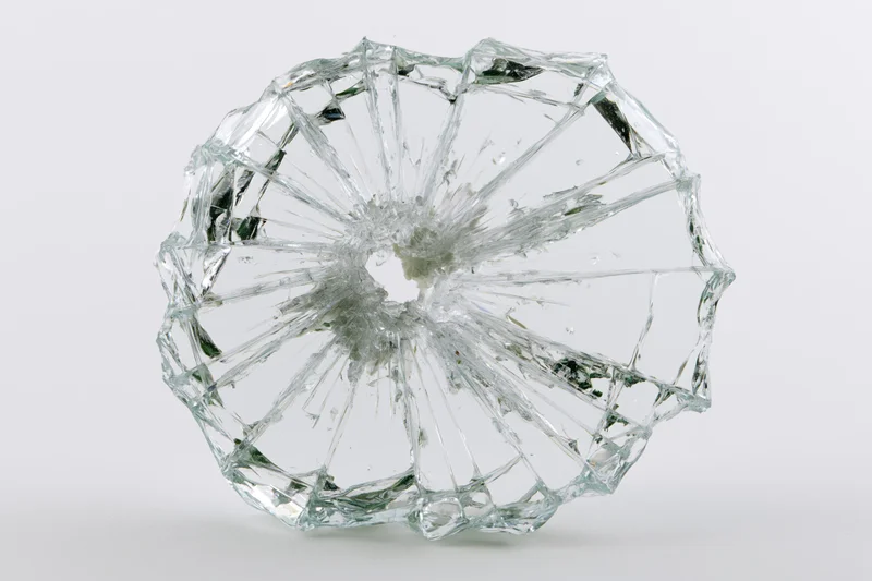 Shattered glass pane with radial cracks from central impact point on white background