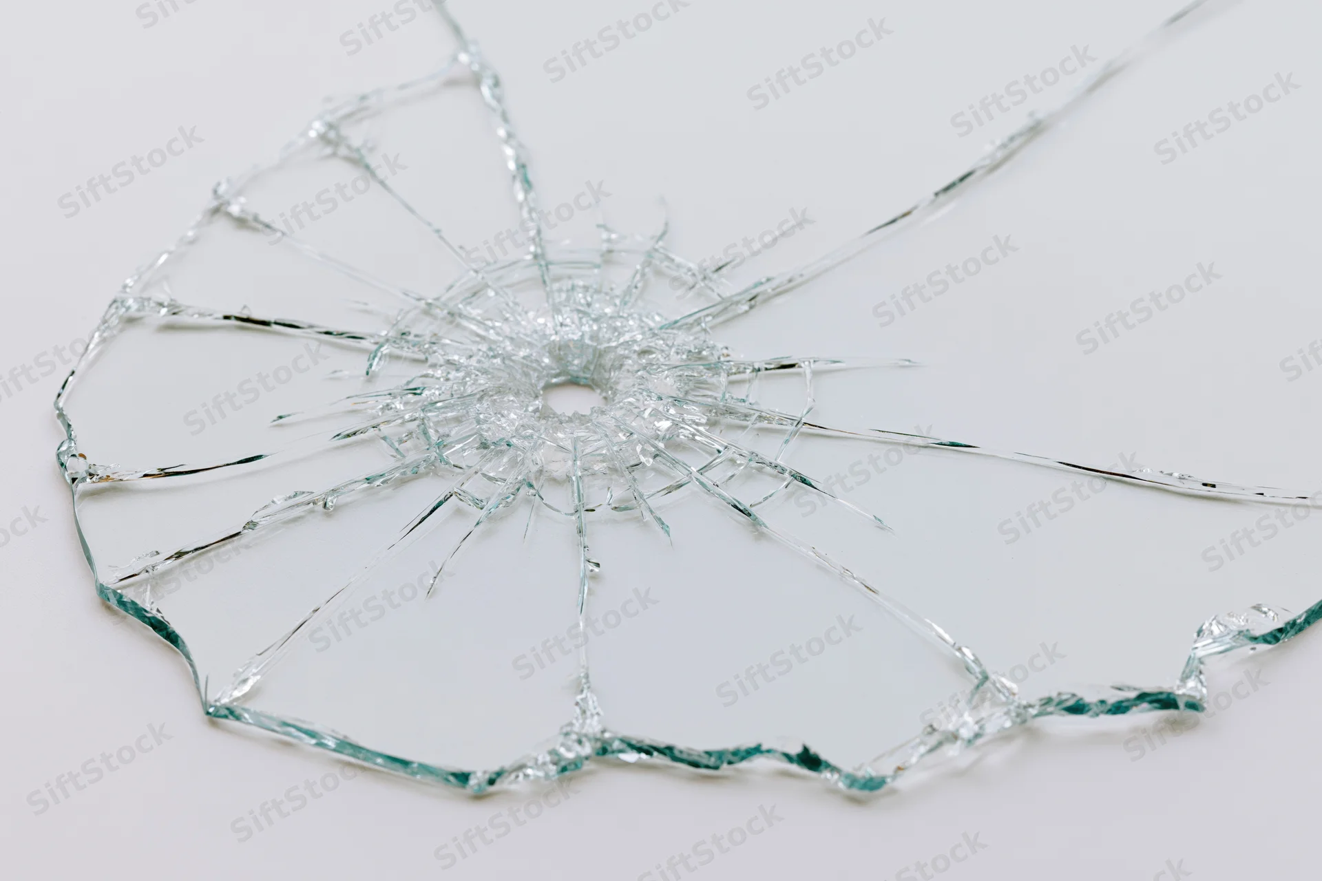 Shattered glass pane with radial cracks from central impact point on white background