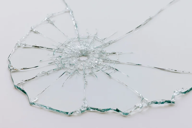 Shattered glass pane with radial cracks from central impact point on white background