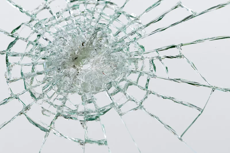 Shattered glass pane with radial cracks emanating from central impact point against white background