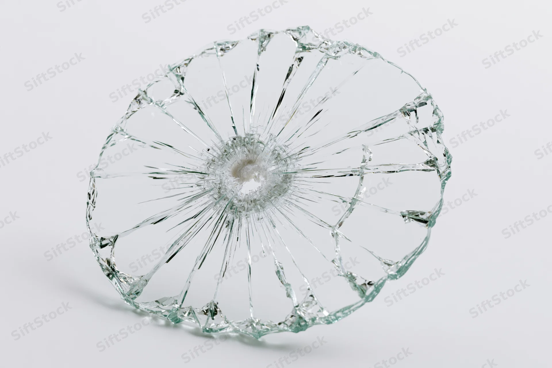 Shattered glass pane with radial cracks from central impact point on white background