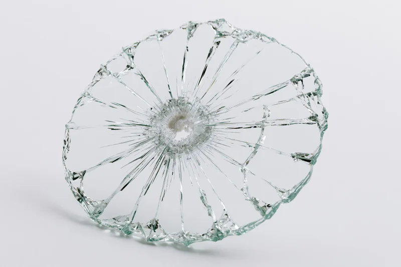 Shattered glass pane with radial cracks from central impact point on white background