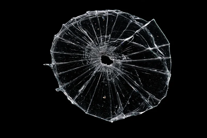 Shattered glass pane with radial cracks from central impact point on black background