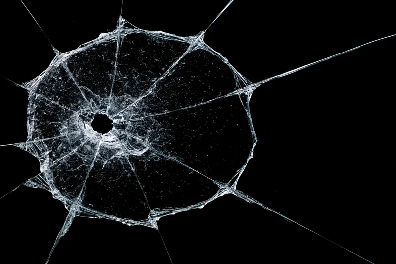 Shattered glass pane with central hole and radial cracks on black background