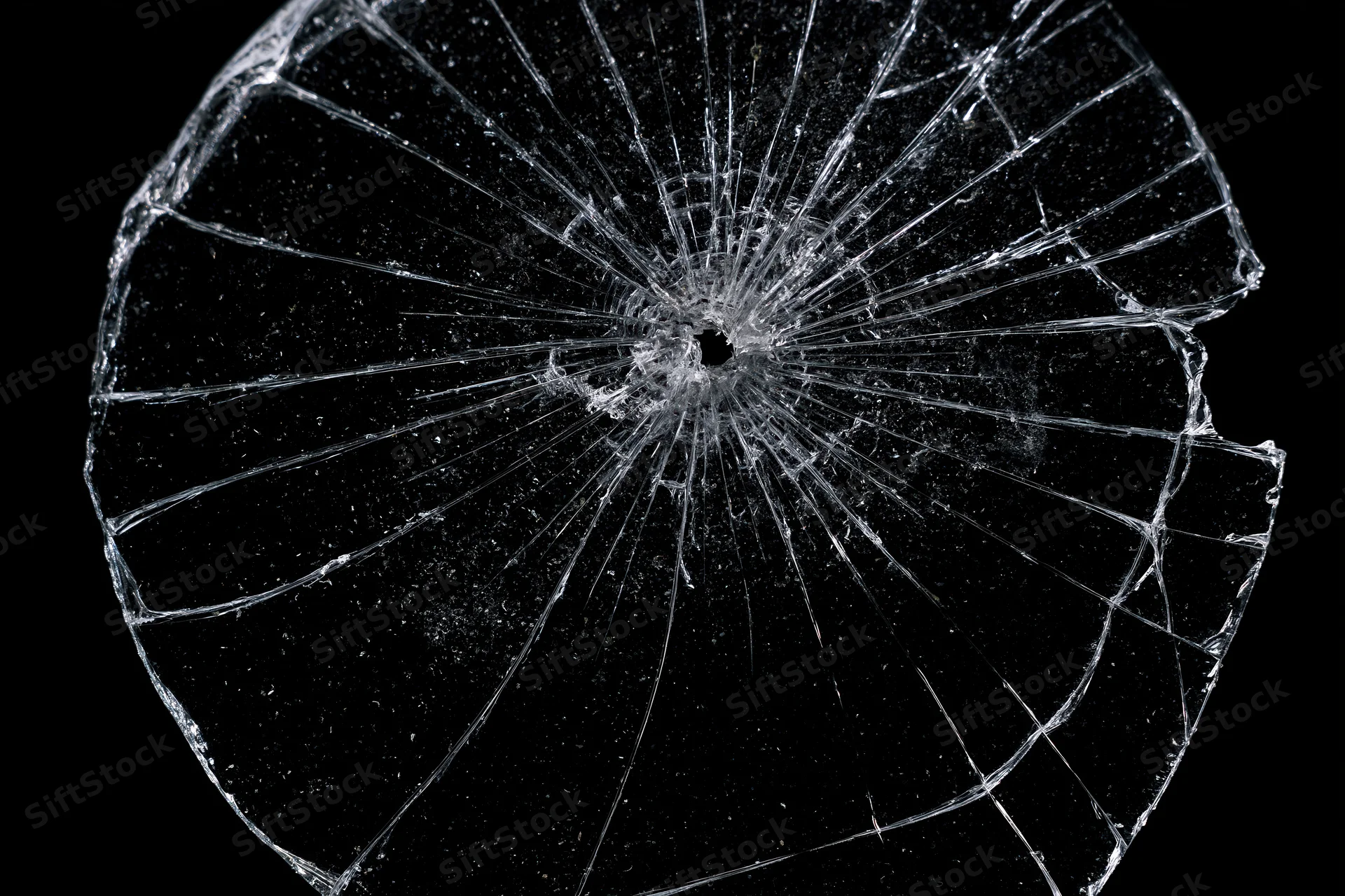 Shattered glass pane with radial cracks from central impact point against black background