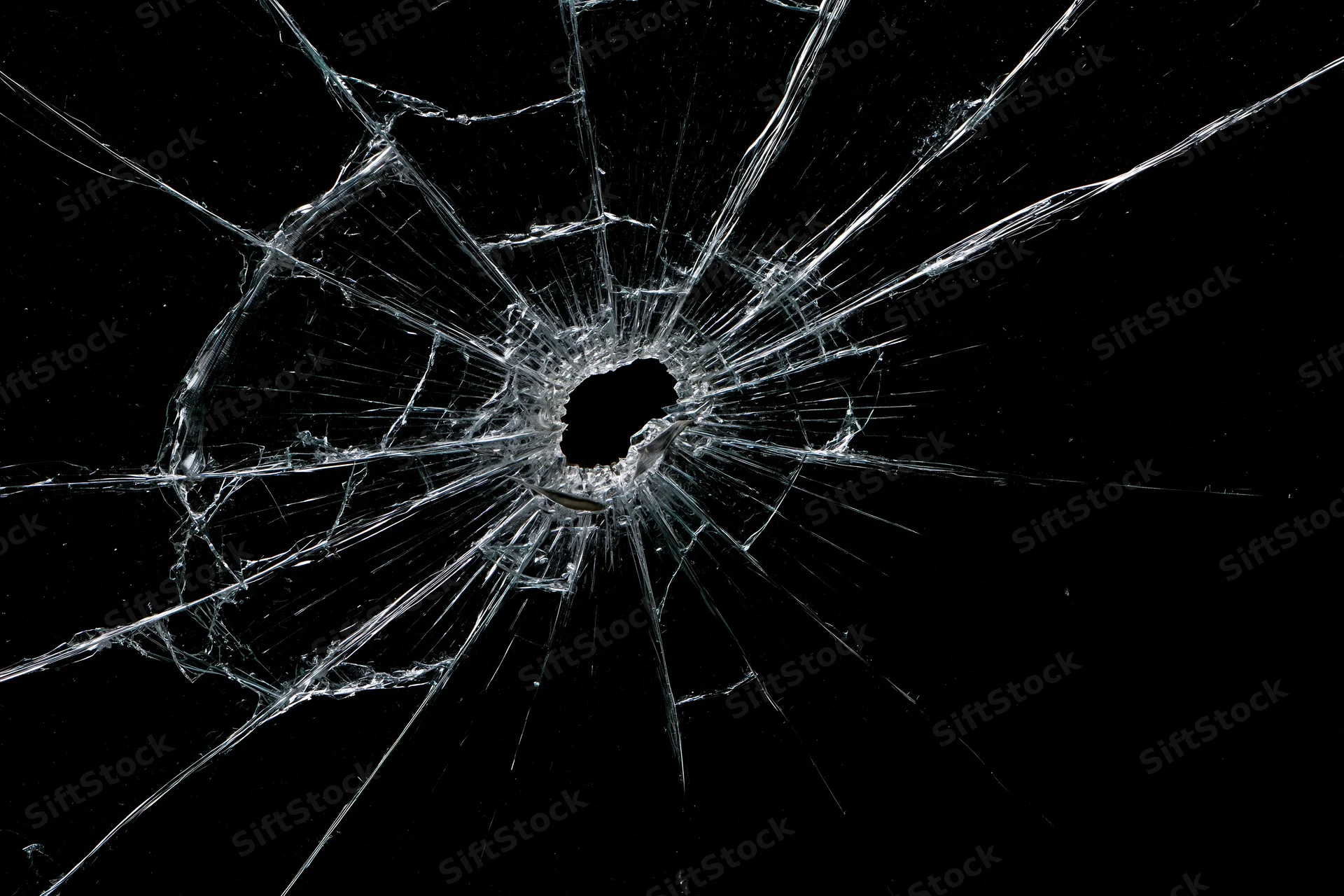 Shattered glass pane with central impact hole radiating cracks against black background