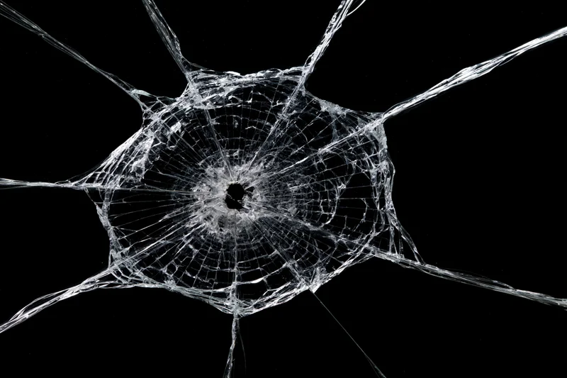 Shattered glass pane with central impact point radiating cracks against black background