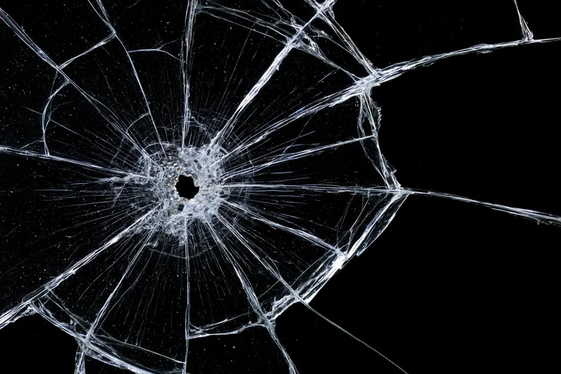 Shattered glass pane with central impact point radiating cracks against black background