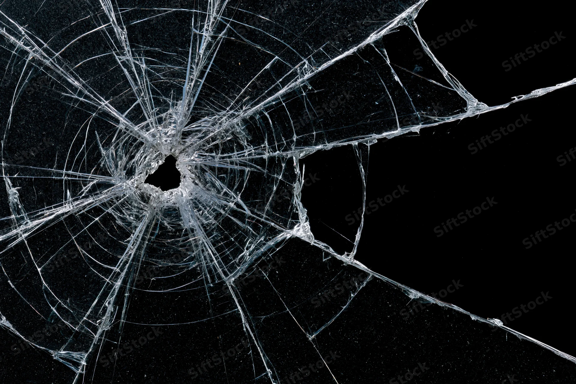 Shattered glass pane with central impact point radiating cracks against black background