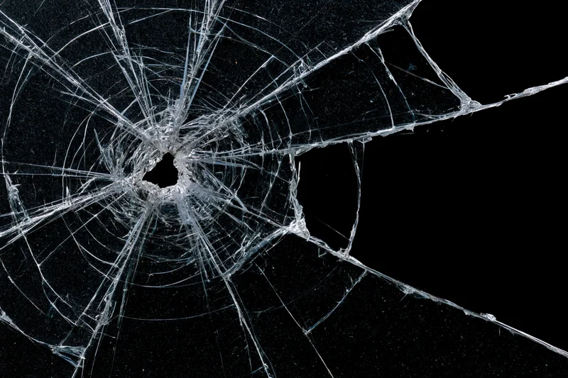 Shattered glass pane with central impact point radiating cracks against black background