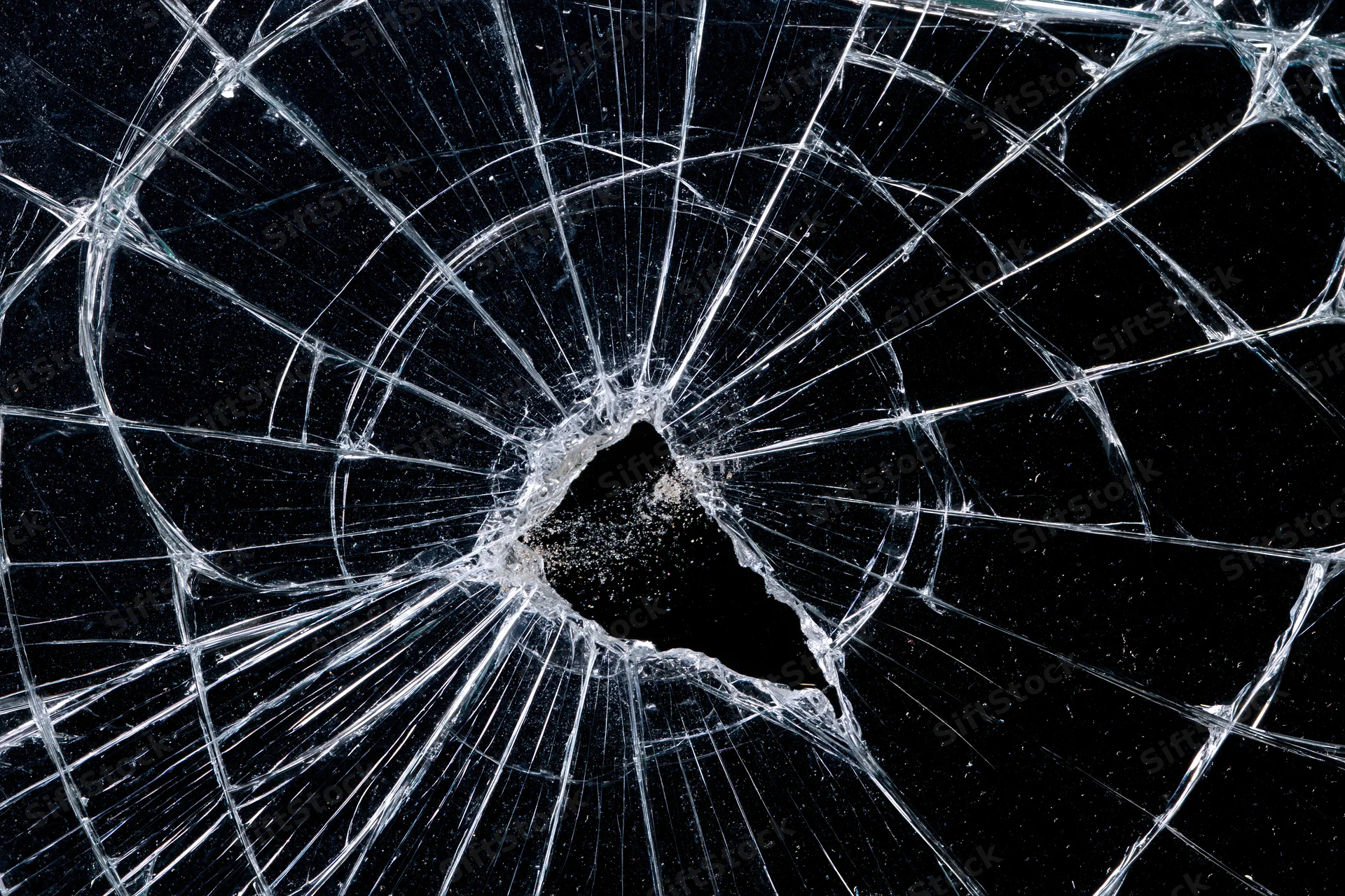 Shattered glass panel with central hole and radiating cracks against black background