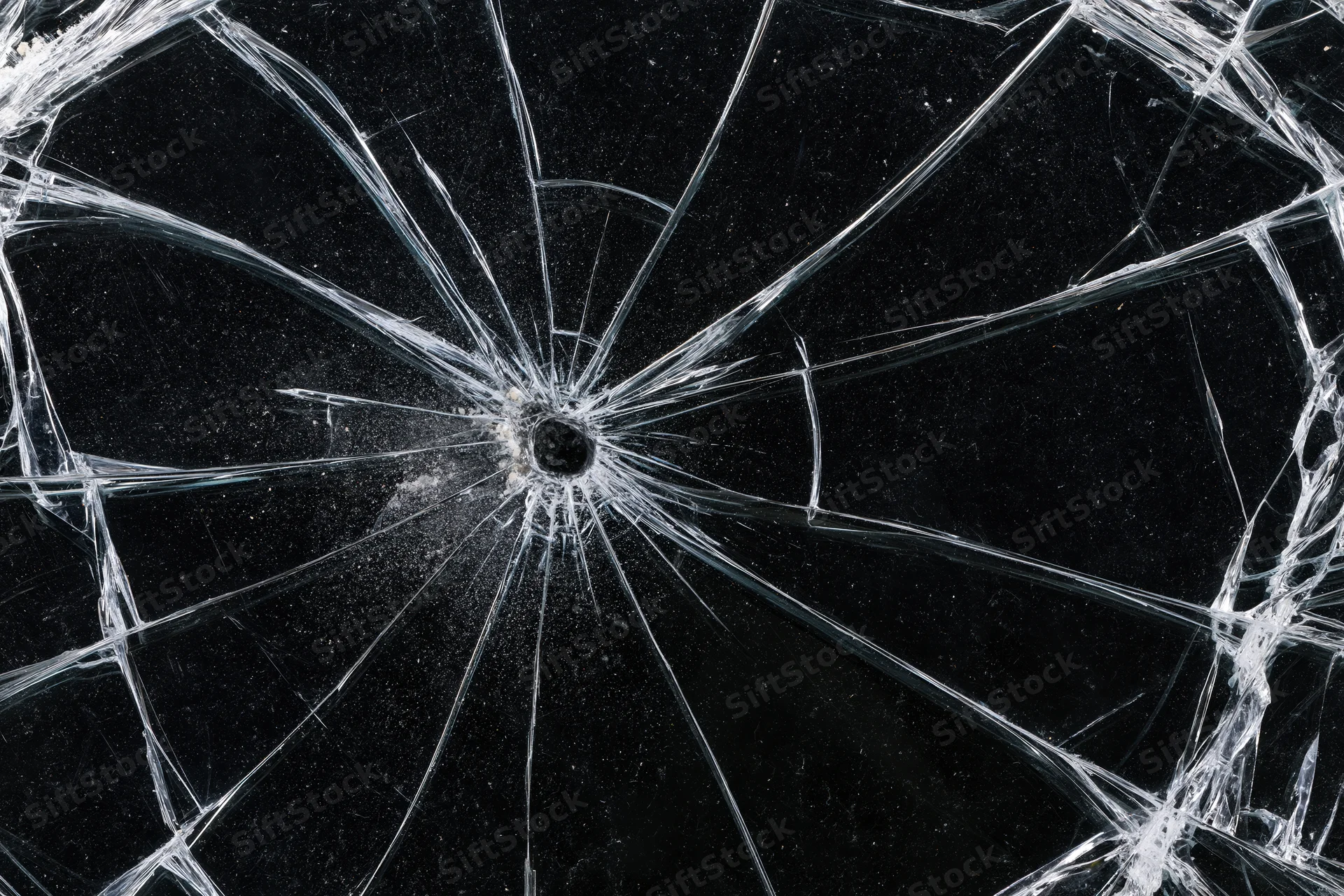 Shattered glass panel with radial cracks from central impact point against dark background