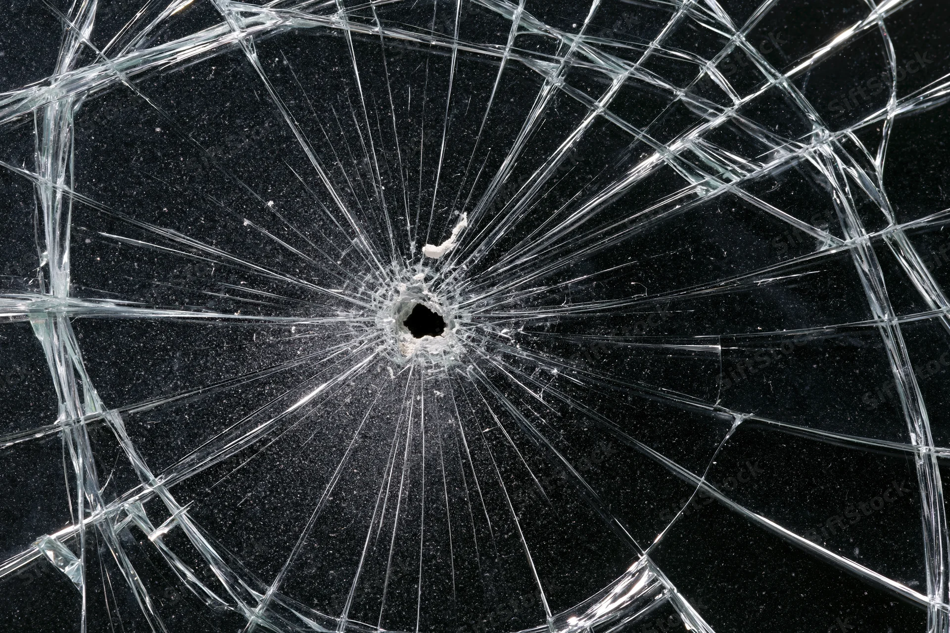 Shattered glass panel with central hole and radial cracks against dark background