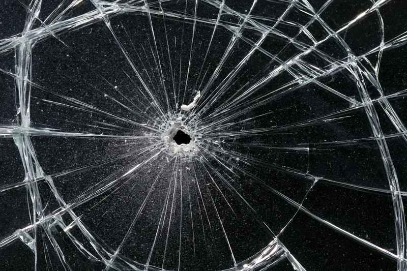 Shattered glass panel with central hole and radial cracks against dark background