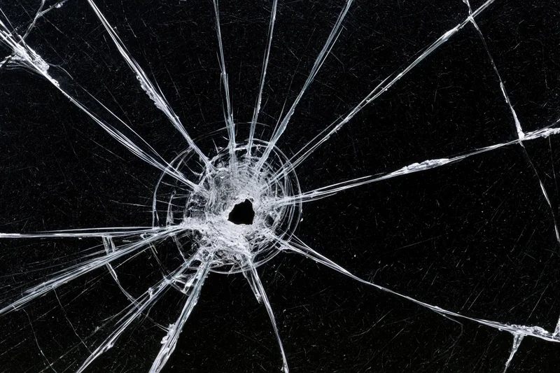 Shattered glass surface with radial cracks from central impact point on black background