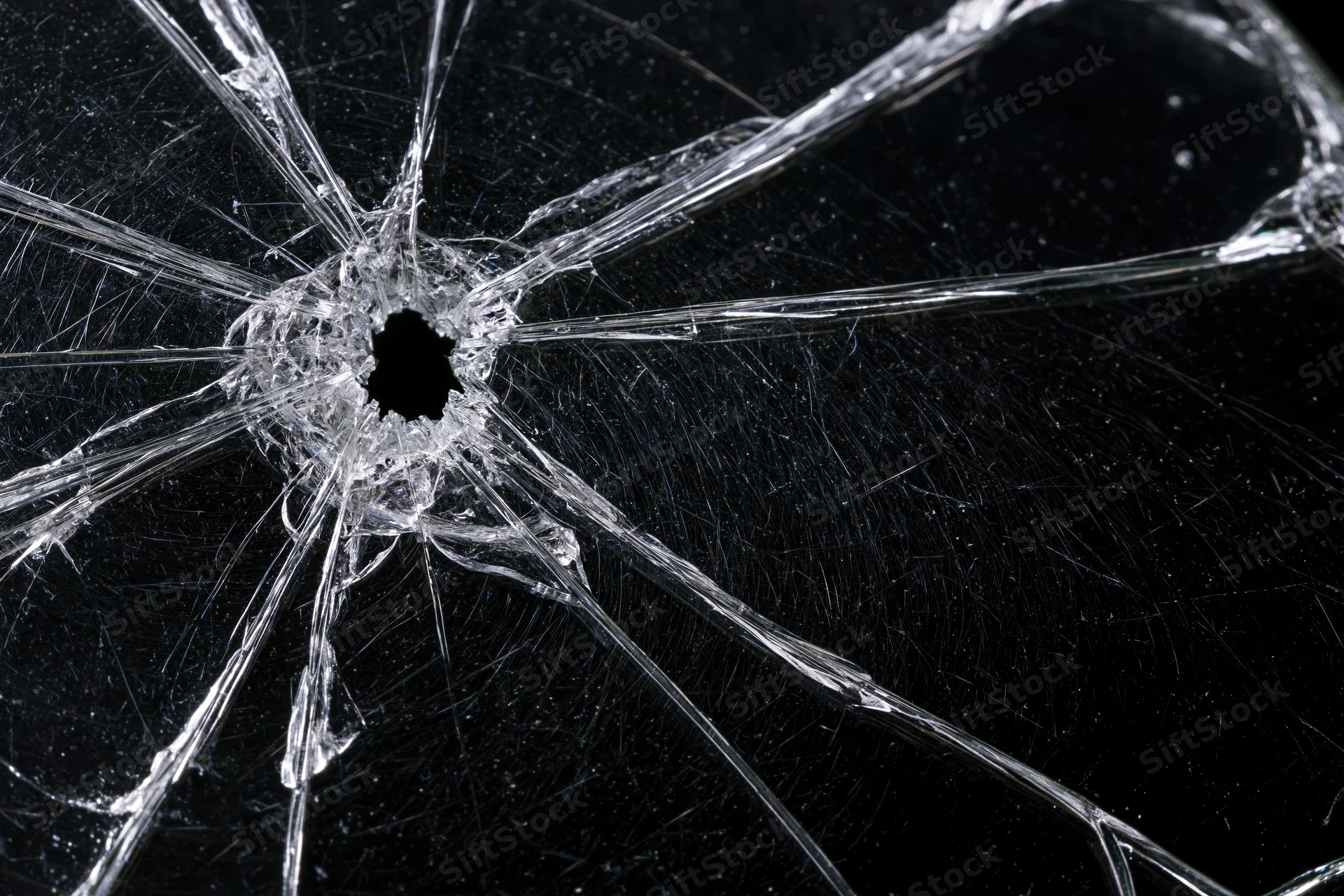 Shattered glass surface with central hole and radial cracks against dark background