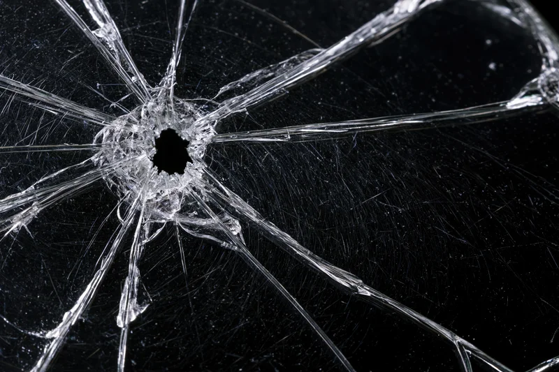 Shattered glass surface with central hole and radial cracks against dark background