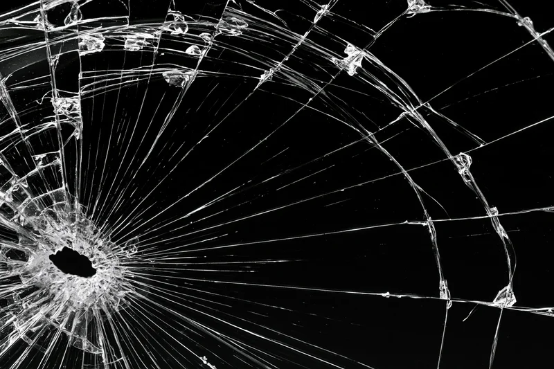 Shattered glass surface with radiating cracks spreading from central hole against black background