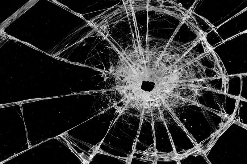 Shattered glass with radial cracks from central impact point on black background