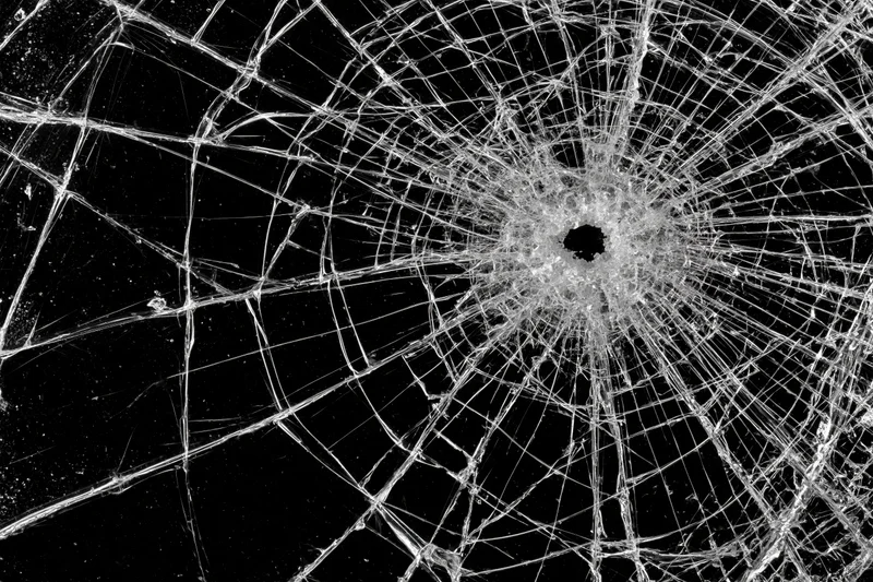 Shattered glass with radial cracks from central impact point on black background