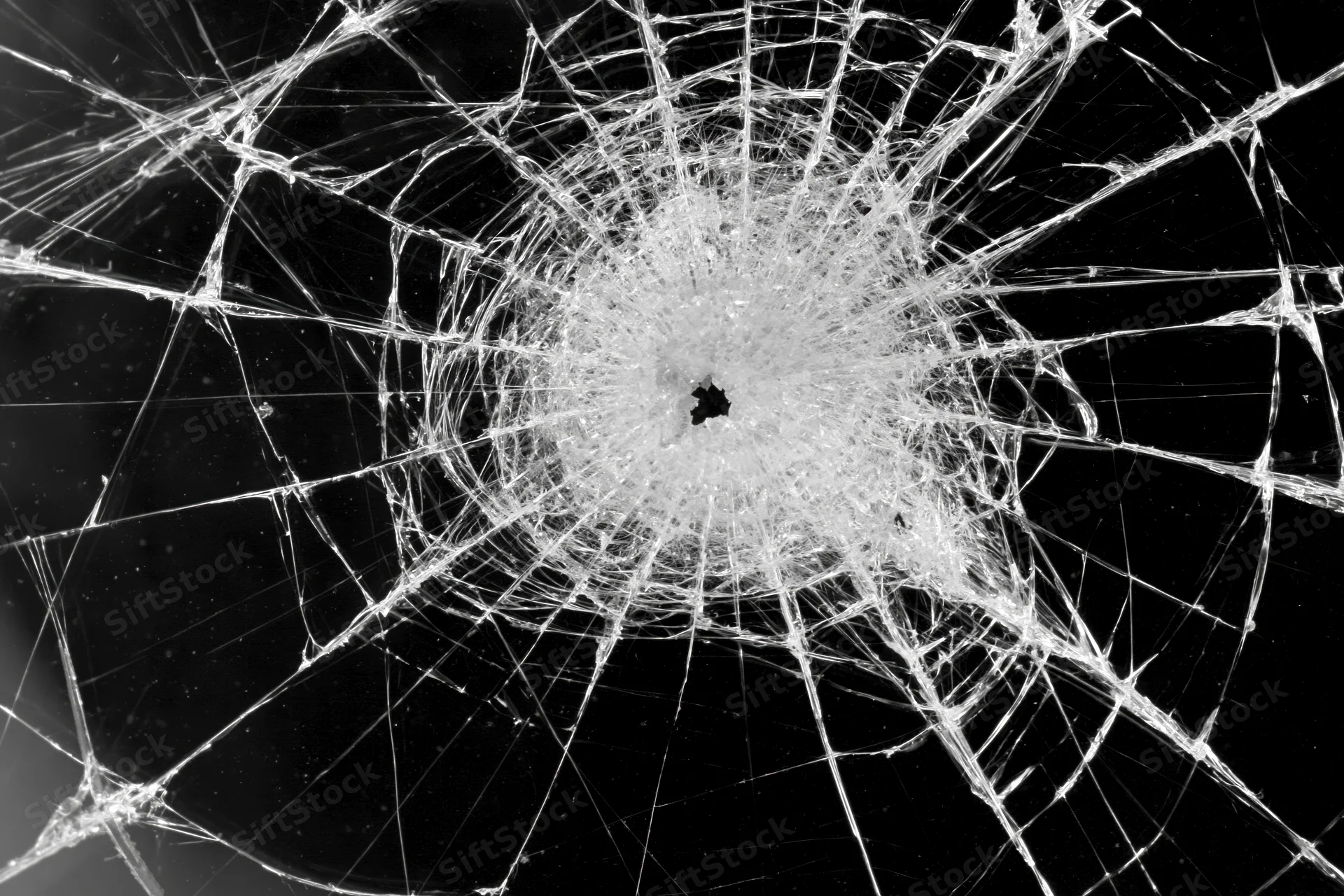 Shattered glass with radial cracks emanating from central impact point against black background