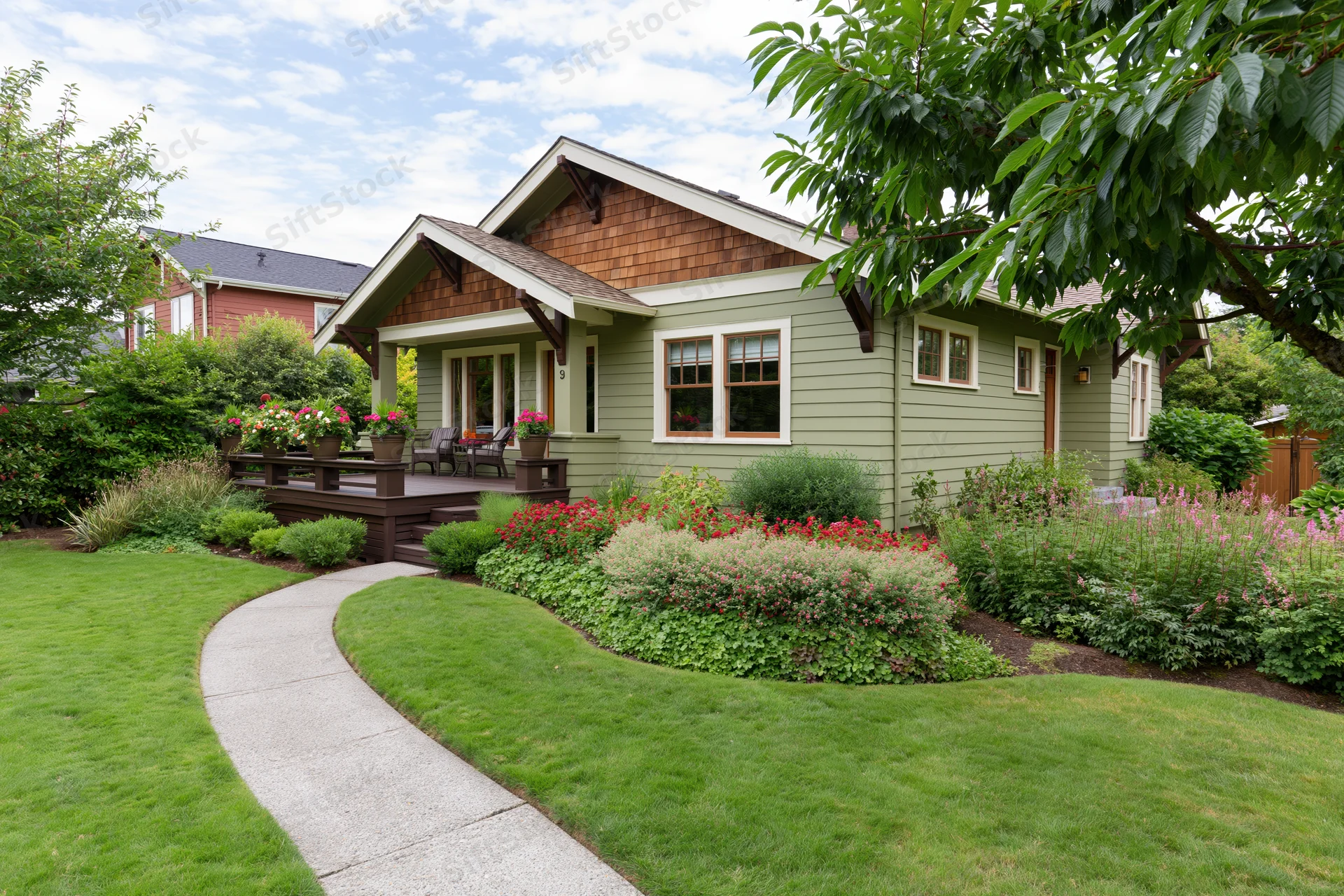 Single-story craftsman house with olive green lap siding and landscaped front yard featuring curved pathway, flower beds, and porch deck