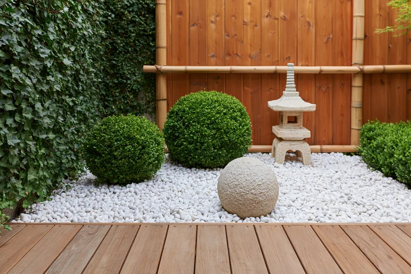 Japanese courtyard garden with stone lantern, trimmed boxwood topiaries, and white gravel on wooden deck