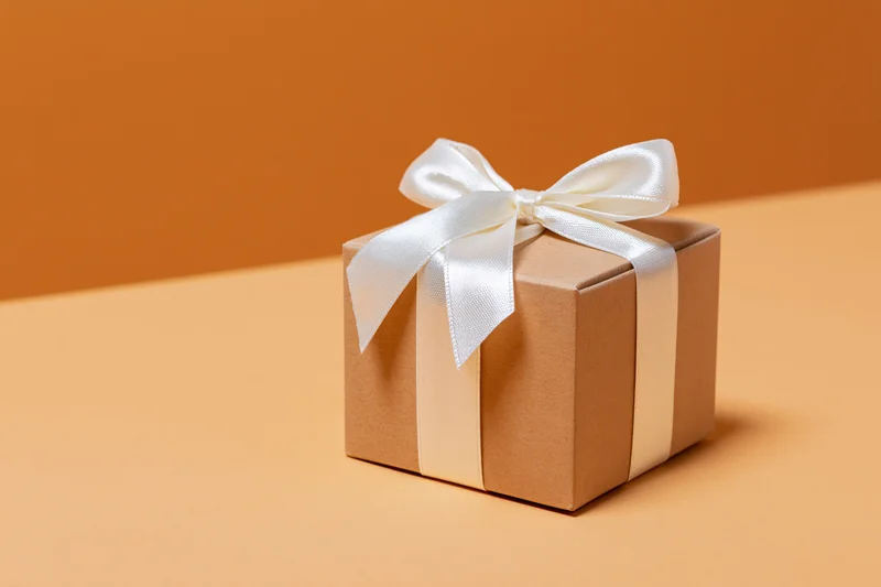 Small kraft cardboard gift box tied with white satin ribbon on orange surface