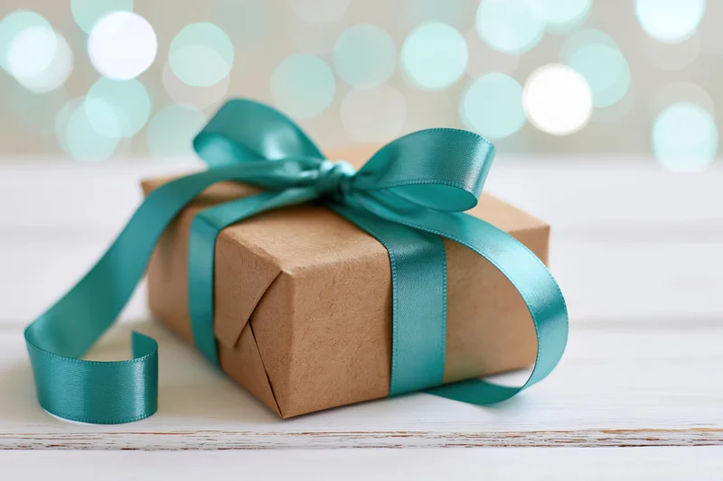 Kraft paper gift box tied with a teal satin ribbon on a white wooden surface