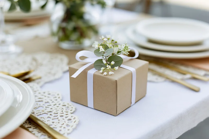 Small kraft paper gift box tied with white ribbon and eucalyptus flowers on a wedding table setting