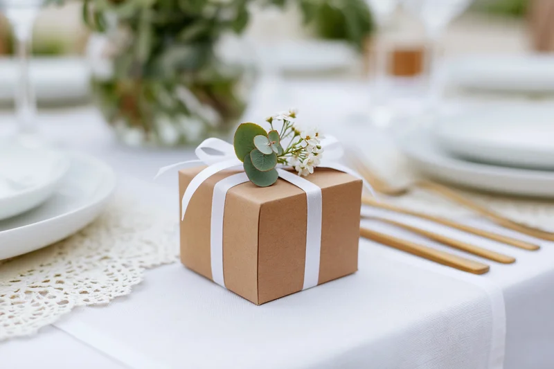 Small kraft paper gift box tied with white ribbon and eucalyptus flowers on a wedding table setting