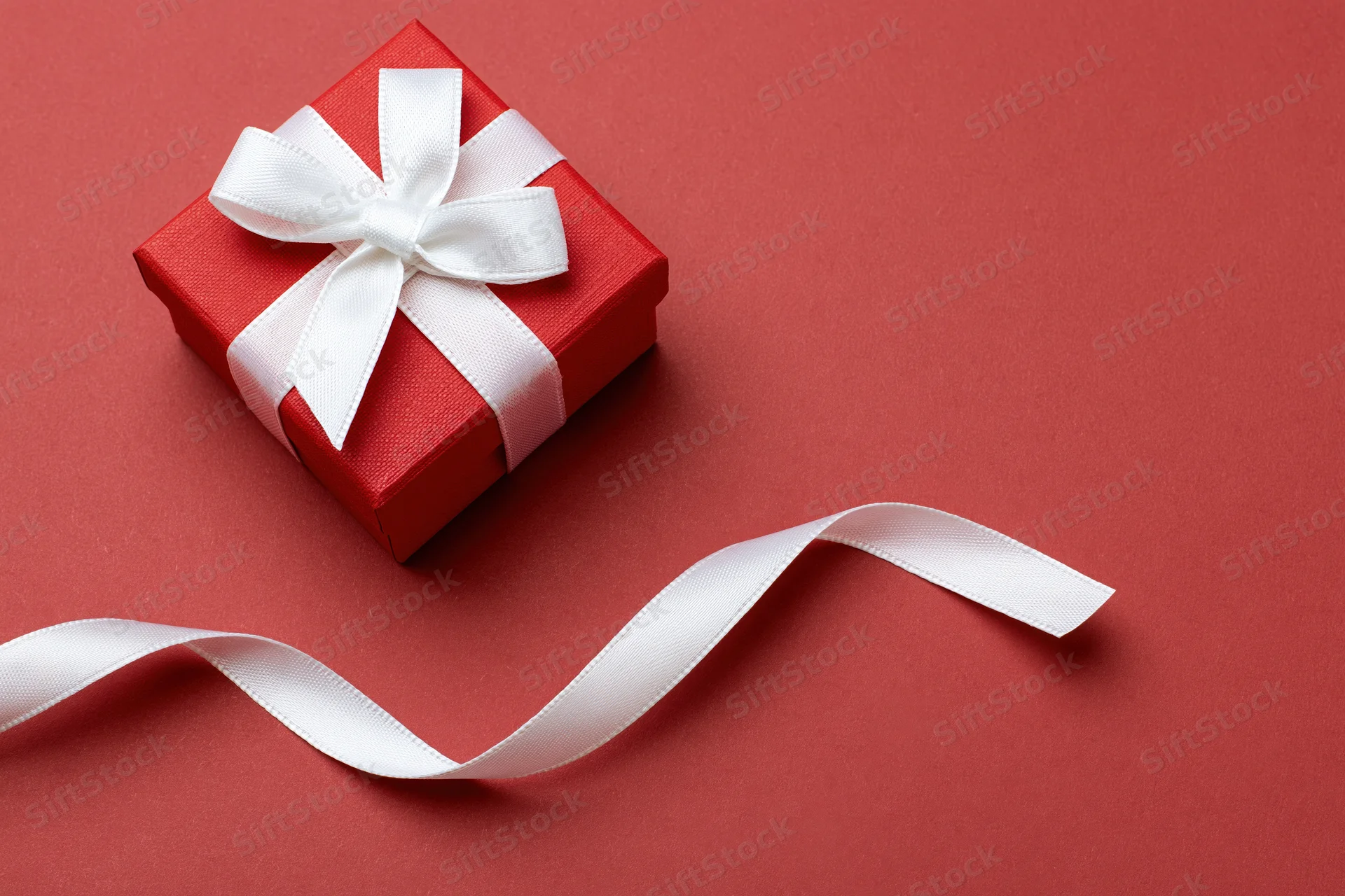 Small red textured gift box with white satin ribbon bow on red background