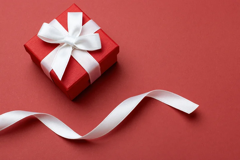 Small red textured gift box with white satin ribbon bow on red background