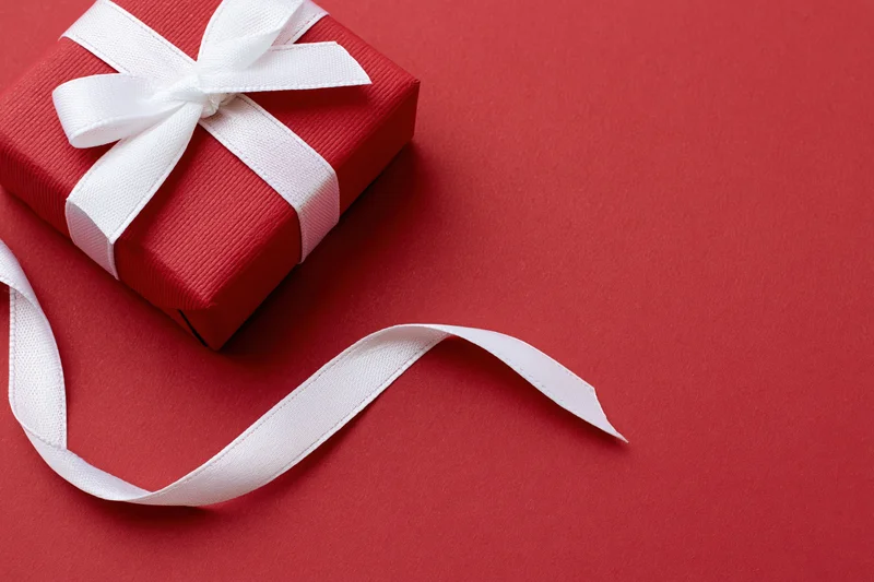 Small red textured gift box with white satin ribbon bow on red surface