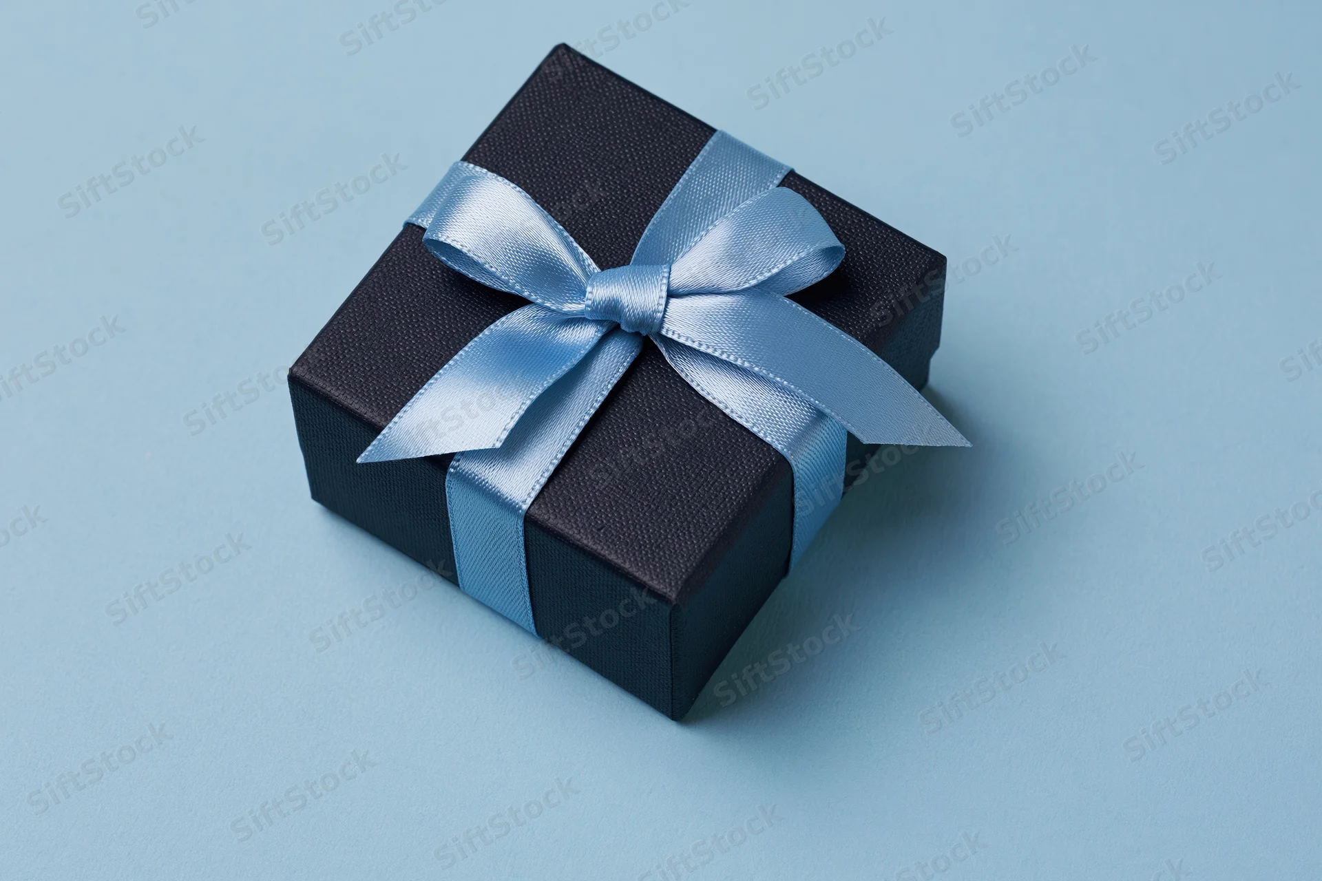 Dark navy gift box with light blue satin ribbon bow on blue background
