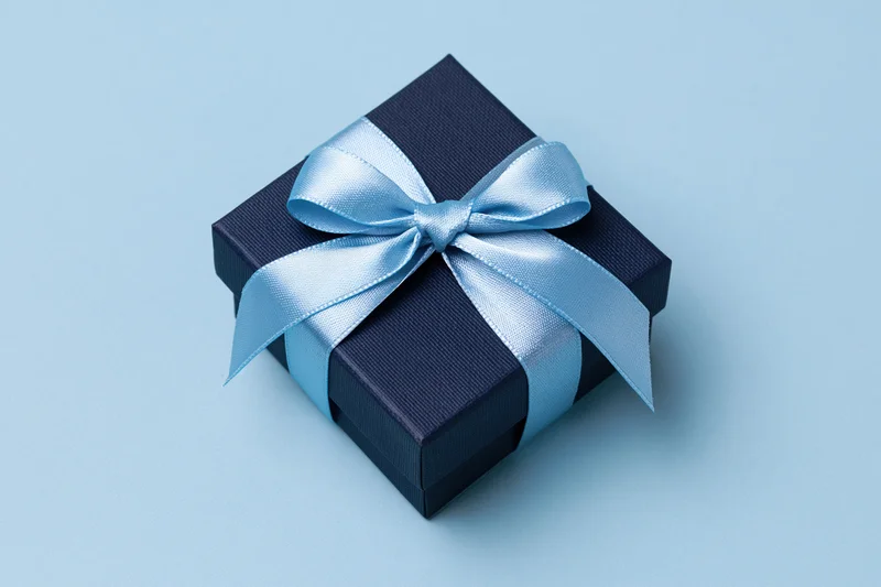 Dark navy gift box with light blue satin ribbon bow on light blue surface