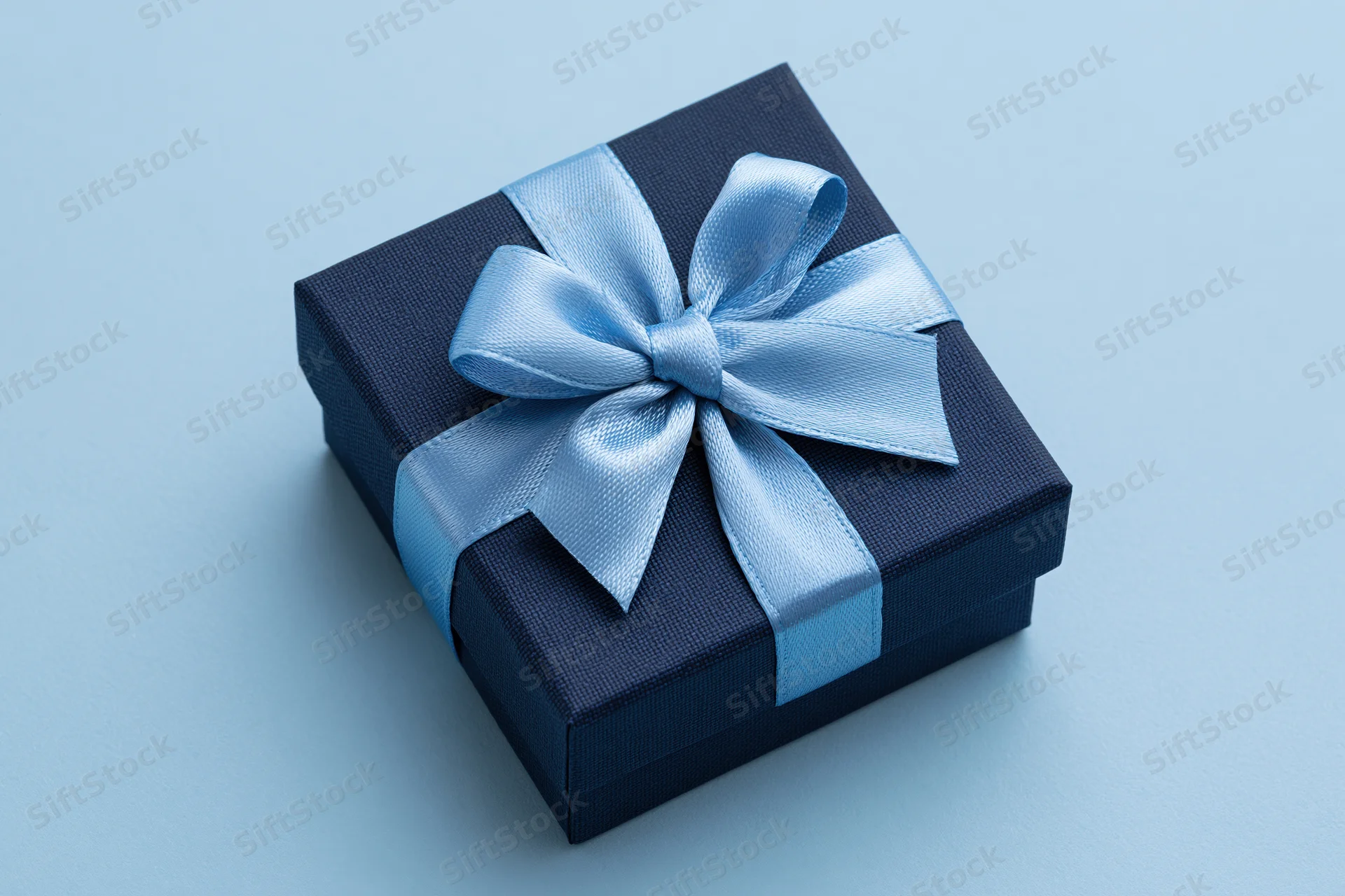 Dark navy gift box with light blue satin ribbon bow on light blue surface