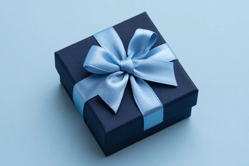 Dark navy gift box with light blue satin ribbon bow on light blue surface