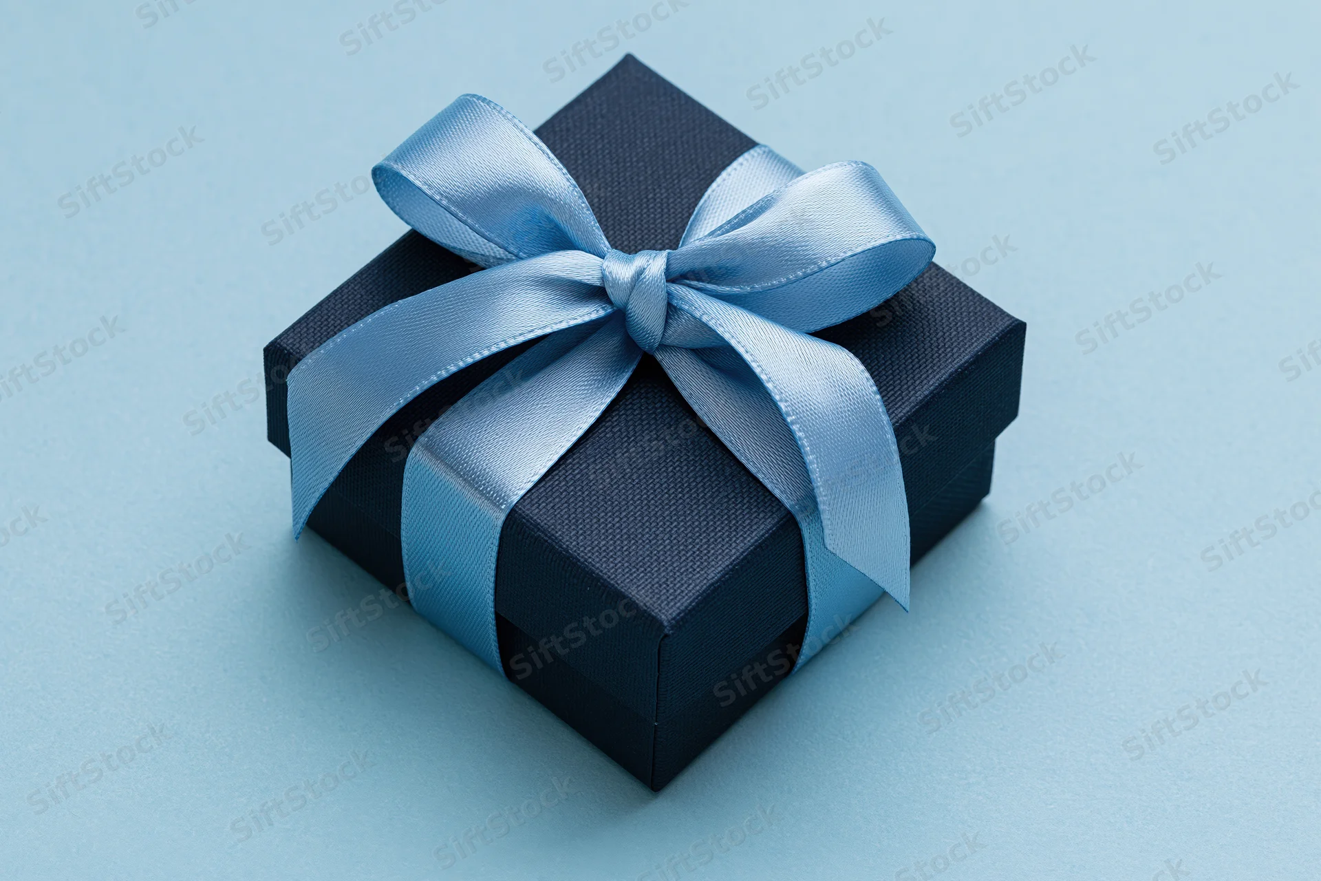 Dark navy gift box with light blue satin ribbon on blue background
