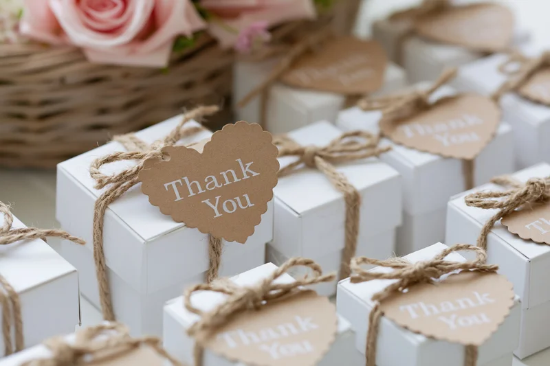 Small white gift boxes tied with rustic twine and kraft paper heart tags reading thank you arranged for a wedding or party favor display